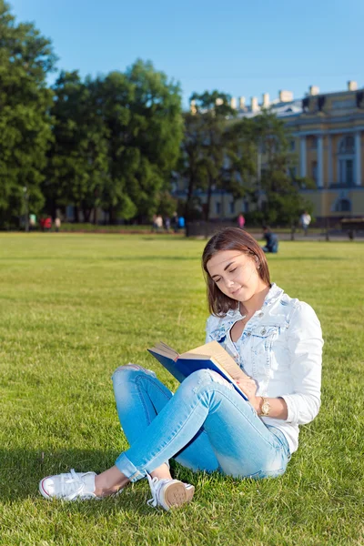 Studentin sitzt auf Rasen und liest Schulbuch. — Stockfoto