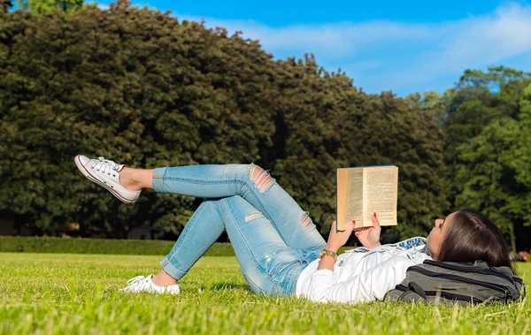 Menina-estudante sentar-se no gramado e lê livro didático . — Fotografia de Stock