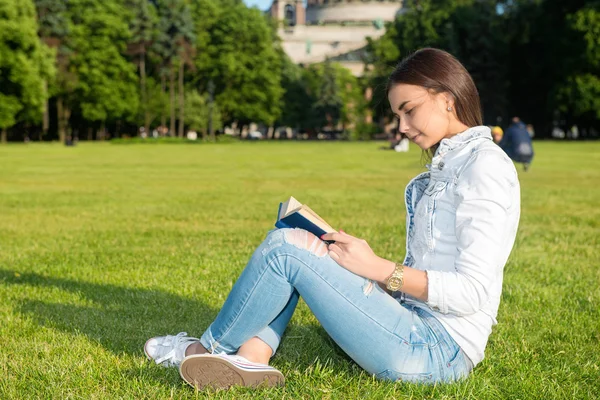 Studentin sitzt auf Rasen und liest Schulbuch. — Stockfoto