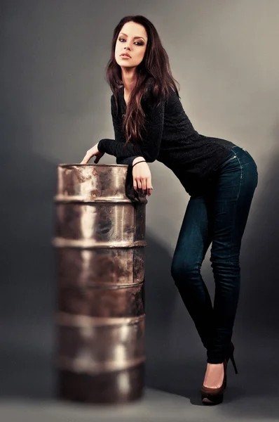 Девушка в джинсах, стоящая возле железной бочки — стоковое фото