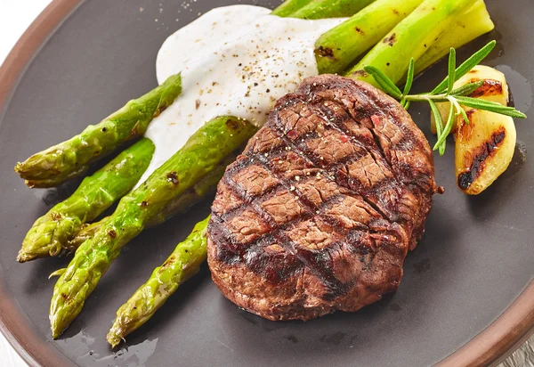 Grilled beef steak and asparagus on dark plate — Stock Photo, Image