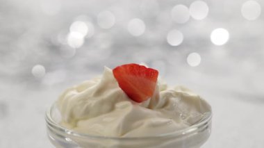 Çilek parçaları gümüş bir bokeh şenlik arka planında çırpılmış mascarpone kremine düşer.