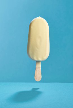 Mavi arka planda beyaz çikolatayla kaplanmış havada duran dondurma.