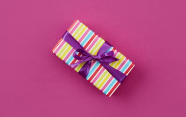 Pembe kağıt zemin üzerinde mor kurdele ile paketlenmiş hediye kutusu, üst görünüm