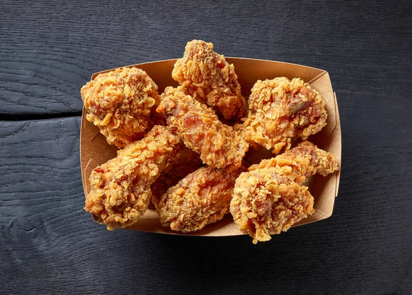 paper take away box of fried chicken wings on black wood background, top view
