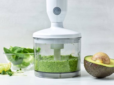 Avokado, kereviz ve plastik şeffaf blender kabında ıspanak. Mutfak masasında sağlıklı kahvaltı içeceği yapmak için.