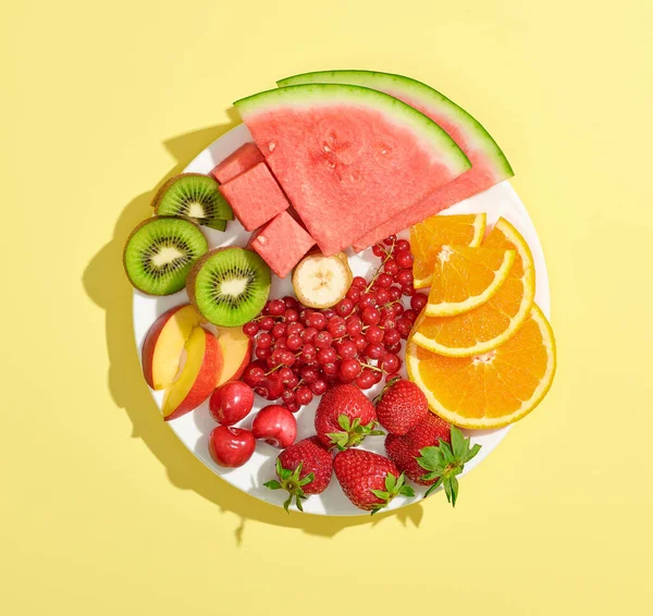 黄色の背景に隔離された様々なスライスされたカラフルな果実と果実のプレートトップビュー — ストック写真