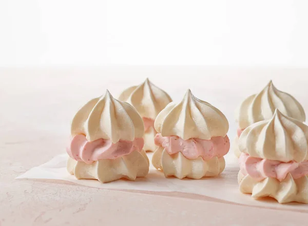 small meringue cakes made from egg whites cookies and strawberry cream on pink background