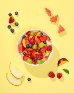 Sarı arka planda bir kase taze meyve salatası.