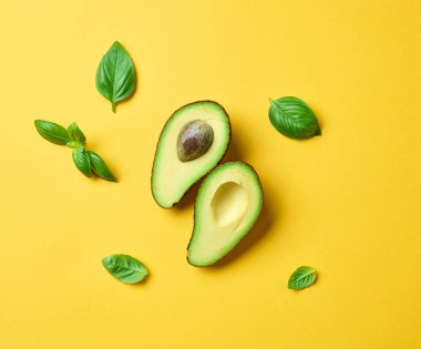Sarı arka planda taze avokado ve fesleğen yaprakları.