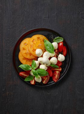 Siyah ahşap mutfak masasında domates ve mozzarella salatası.