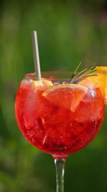 İnsan eli bir bardak klasik kırmızı spritz kokteyli al, yeşil yaz bahçesi arka planı.