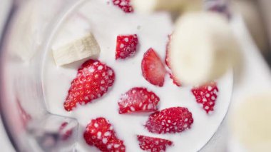 Sağlıklı kahvaltı içeceği, milkshake malzemeleri yakın çekim için, hafif mutfakta ağır çekimde yiyecekler için kesilmiş çilek ve sütle karıştırılmış çilek kabına düşen taze çiğ muz parçaları.