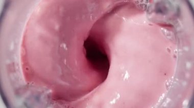 Çilekli ve muzlu, pembe milkshake karışımı. Üst Manzara. Ağır çekim. Sağlıklı protein içeceği konsepti, yiyecek yakın çekimi. Protein tozu kaşıktan meyve suyuna dökülüyor.