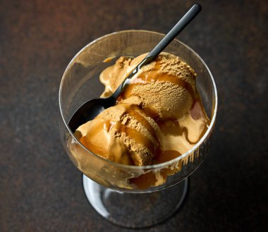 caramel ice cream scoop with sauce served in glass on dark brown table background