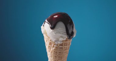 Erimiş çikolata sosu bir kepçe vanilyalı dondurmanın üzerinden mavi bir külahta akıyor. 