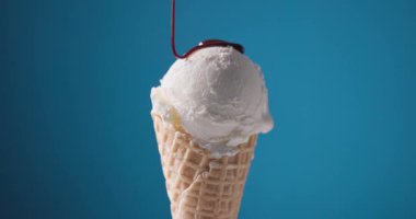 Erimiş çikolata sosu bir kepçe vanilyalı dondurmanın üzerinden mavi bir külahta akıyor. 