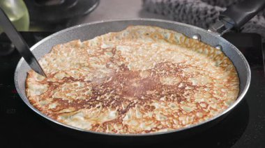 Aşçı, mutfakta spatulayla taze pişmiş krepi sıcak tavadan kaldırır. Sağlıklı kahvaltı için evde leziz krep yapma süreci, yiyecek kapanıyor.