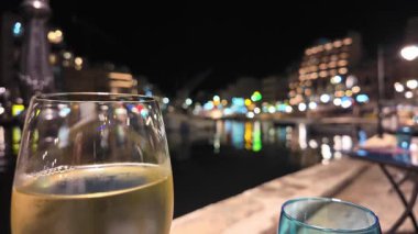 Arka planda şarap kadehleri, çözünmüş su ve gece lambaları var. Malta, Spinola Körfezi, St Julians Körfezi 'ndeki açık deniz restoranı masası.