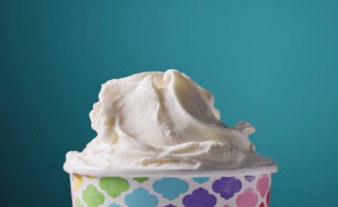 Kağıt bardakta beyaz vanilyalı dondurma, mavi arka planda yiyecek.