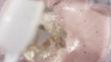 Çilekli ve muzlu, pembe milkshake karışımı. Üst Manzara. Ağır çekim. Sağlıklı protein içeceği konsepti, yiyecek yakın çekimi. Protein tozu kaşıktan meyve suyuna dökülüyor.