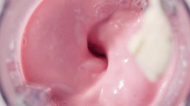 Çilekli ve muzlu, pembe milkshake karışımı. Üst Manzara. Ağır çekim. Sağlıklı protein içeceği konsepti, yiyecek yakın çekimi. Protein tozu kaşıktan meyve suyuna dökülüyor.