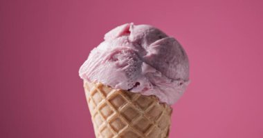 Waffle külahında bir kepçe çilekli dondurma pembe arka planda dönüyor, yiyecek yakın plan