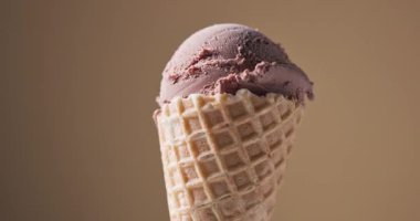 Kahverengi arka planda dönen waffle külahında bir kepçe çikolatalı dondurma.