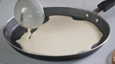 Kek hamuru kepçeyle sobanın üstüne dökülüyor. Mutfakta ev yapımı krep yapmak için pişirme işlemine yakın çekim