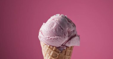 Krep külahında bir kepçe çilekli dondurma pembe bir zemin üzerinde dönüyor. Dondurma topunun üzerine şeker serpiştiriyor. 