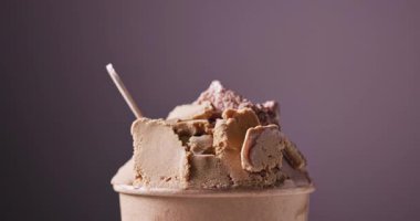 Çikolata ve fıstık dondurması kağıt bardakta dönüyor, yemekler mor arka planda kapanıyor.