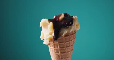 Çikolata sosu sarı mango ve waffle külahında ananas şerbeti üzerine akar. Renkli arka planda açılır, yemek yakın planda kalır.