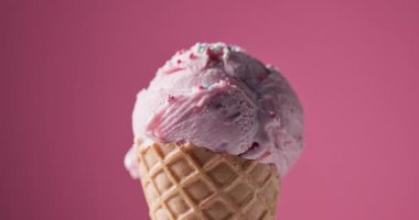 Krep külahında bir kepçe çilekli dondurma pembe bir zemin üzerinde dönüyor. Dondurma topunun üzerine şeker serpiştiriyor. 