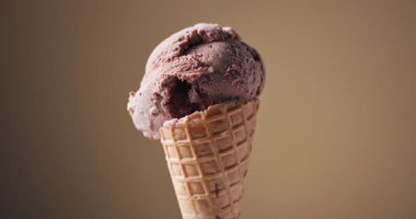 Kahverengi arka planda dönen waffle külahında bir kepçe çikolatalı dondurma.