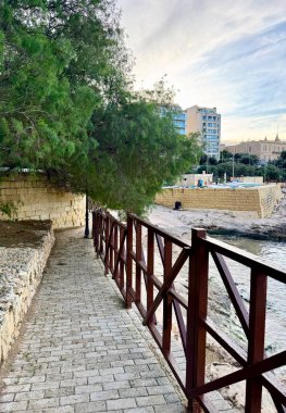Körfez kıyısı boyunca yürüme yolu olan güzel bir Malta manzarası ve arka planda modern yüksek binalar, Sliema