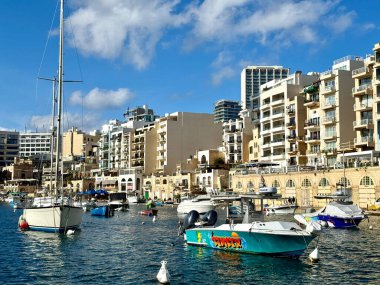 St. Julian 's, Malta - 23 Kasım 2025: St. Julians ve Spinola körfezine demirlemiş küçük balıkçı tekneleri, Malta' nın başkenti St. Julians 'ta güneşli bir günde. St Julian, Malta 'da popüler bir turizm merkezidir.