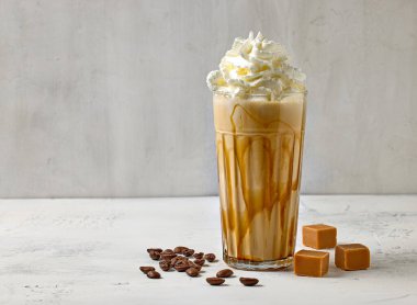 Bir bardak karamel sütlü kahve. Süslü krema ve beyaz masa.