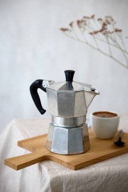 Kahve demliği ve bej masa arkasında bir fincan espresso.
