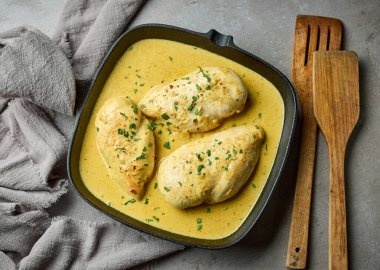 Gri mutfak arka planında, krema soslu leziz tavuk göğsü eti. Sağlıklı öğle yemeği için hazır.