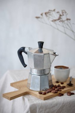 Kahve demliği ve bej masa arkasında bir fincan espresso.