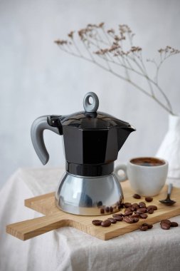 Kahve demliği ve bej masa arkasında bir fincan espresso.