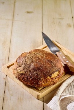 Taze pişirilmiş ev yapımı tatlı ve ekşi çavdar ekmeği. Mutfak kesme tahtasıyla servis ediliyor. Hafif, güneşli, ahşap bir masada bıçakla. Kaba ve doğal besin bileşimi fırın, ev yapımı yemek ve geleneksel mutfak için uygundur.