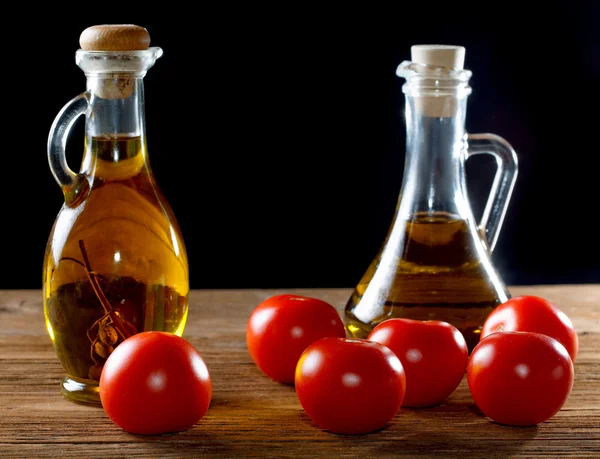 Tomatoes and bottles of olive oil on rustic table — Stock Photo, Image