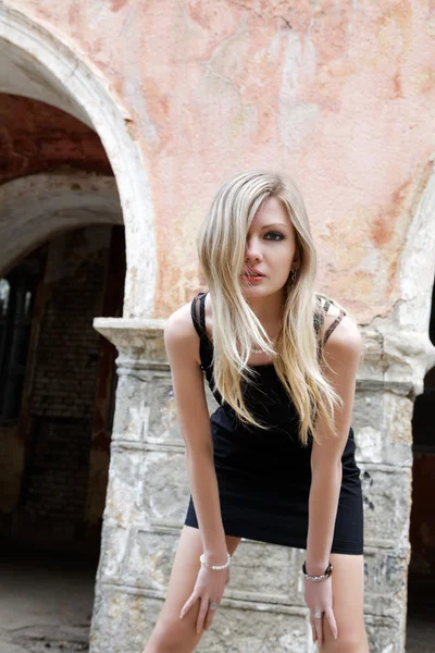 Flickan blondin i en svart klänning på en bakgrund av plas — Stockfoto