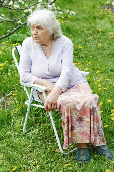 De grootmoeder in de tuin onder een bloeiende appelboom — Stockfoto