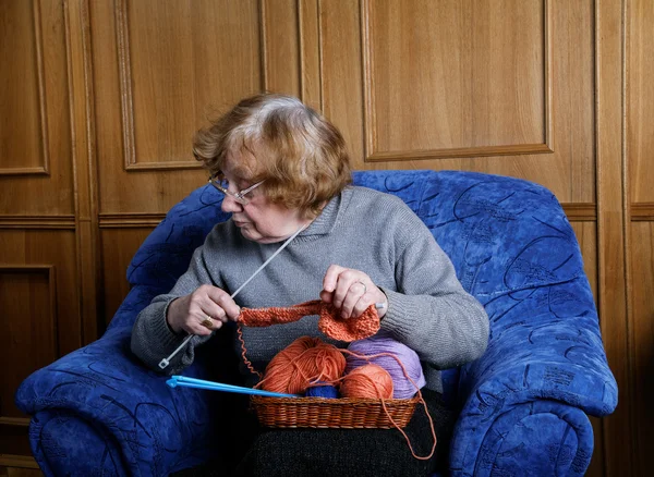 The old woman sits in an armchair and knits — Stock Photo, Image