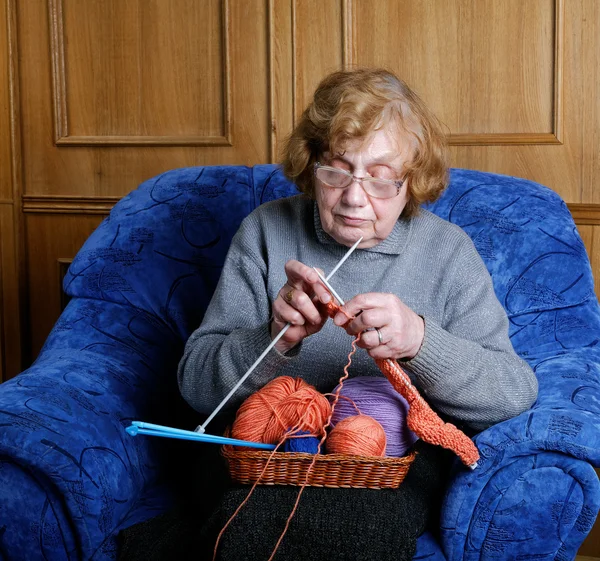 The old woman sits in an armchair and knits — Stock Photo, Image