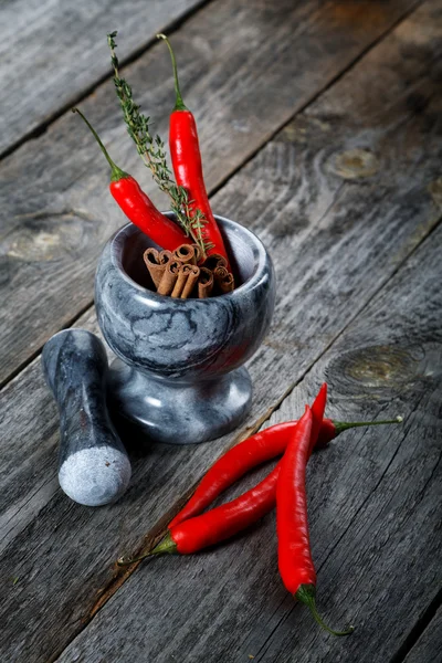 Mortar with cinnamon and chilli pepper on an old table — Stock Photo, Image