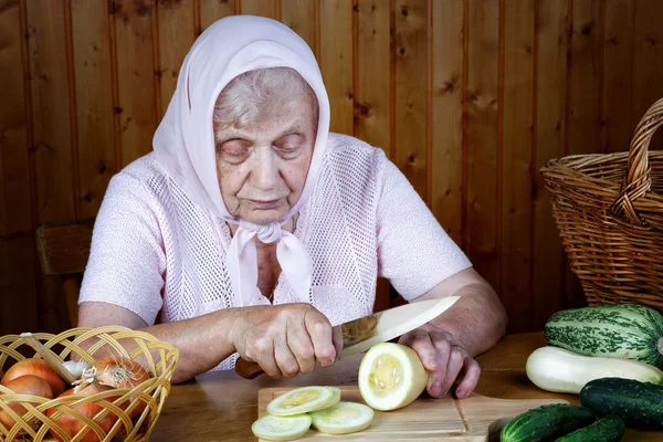 La donna vecchia taglia il midollo vegetale su un tavolo — Foto Stock