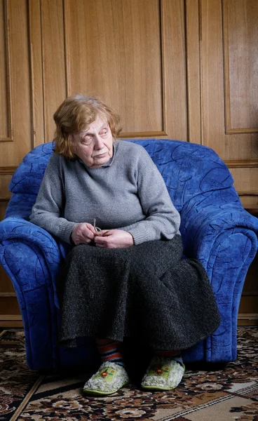 De oude vrouw zit in een leunstoel — Stockfoto